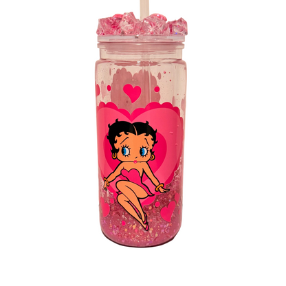 A clear acrylic tumbler with a straw, filled with pink glitter and pink ice, featuring a large pink heart and a cartoon Betty Boop character printed on the front.